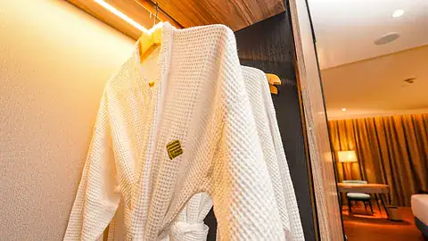 White waffle bathrobe on a wooden hanger in a warmly lit hotel room