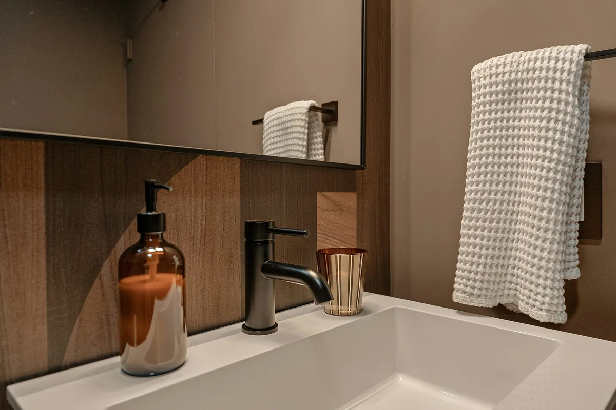White waffle towel hanging on a rail beside a bathroom sink with an amber soap dispenser