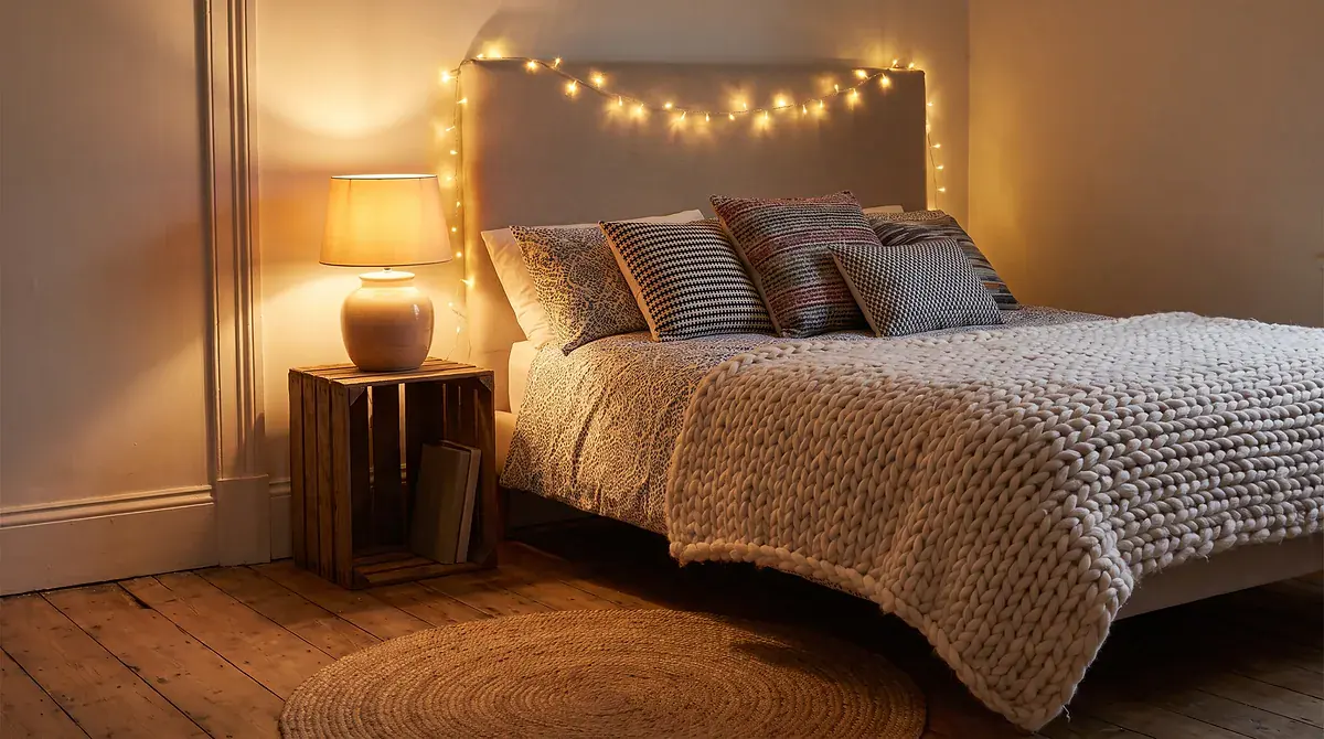 Cozy bedroom with string lights, layered throw pillows and knit blanket